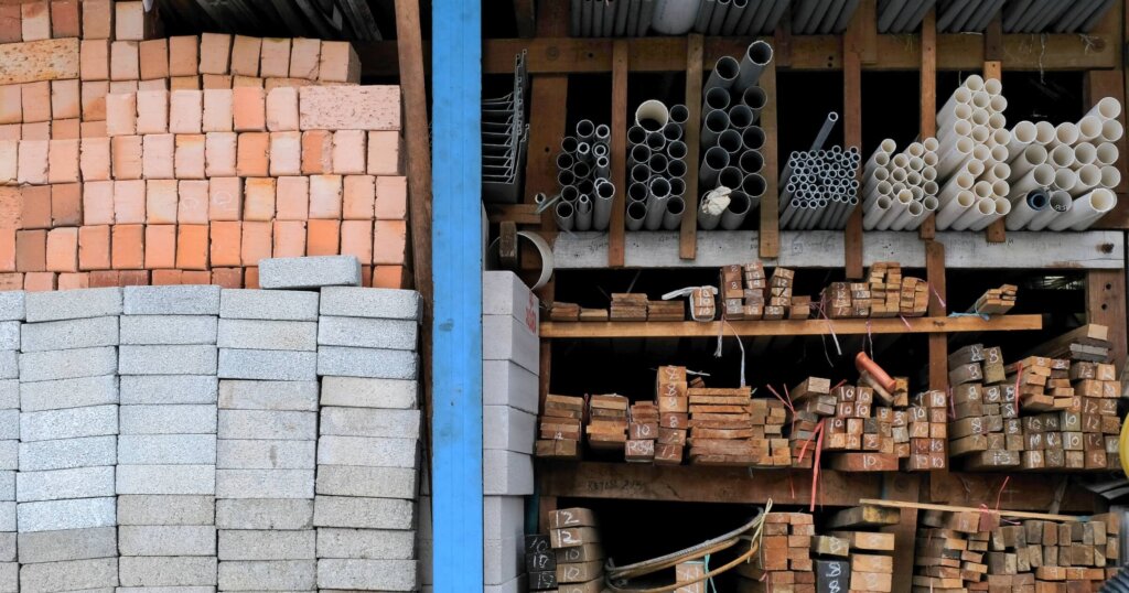 Construction building materials and industrial supplies such as bricks, woods and pipes stacked and arranged for sale at a hardware store front.