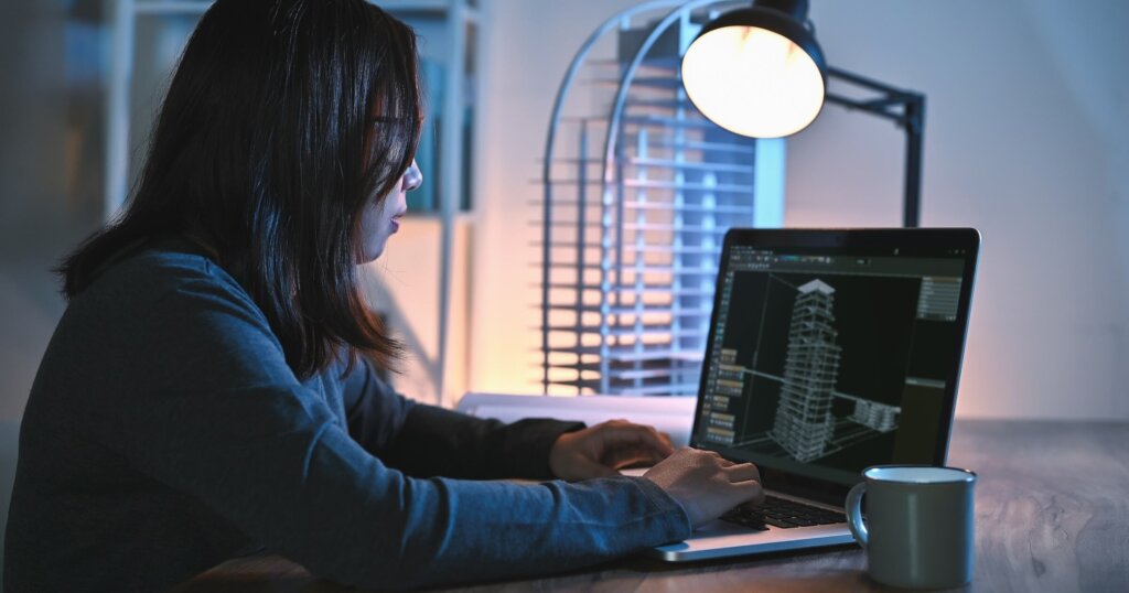 Asian architect or women engineer use laptop study detail and construction design alone in drawing in an office room at night with building model on desks office.
