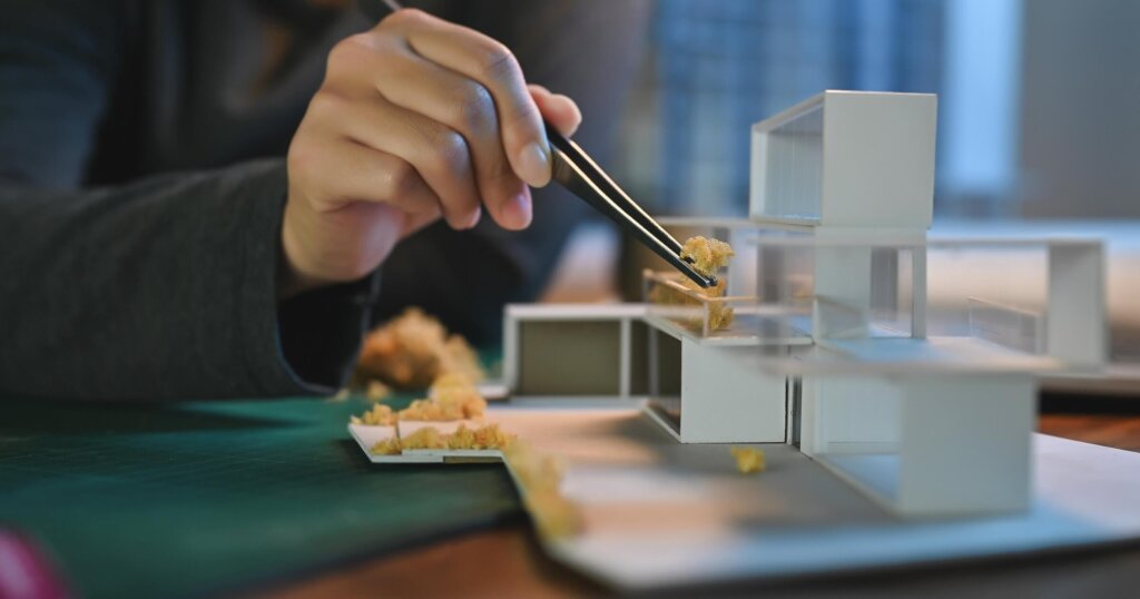 Close-up hand of Architect students diligently make house model building samples with paper art architecture tools at night in their alone room.