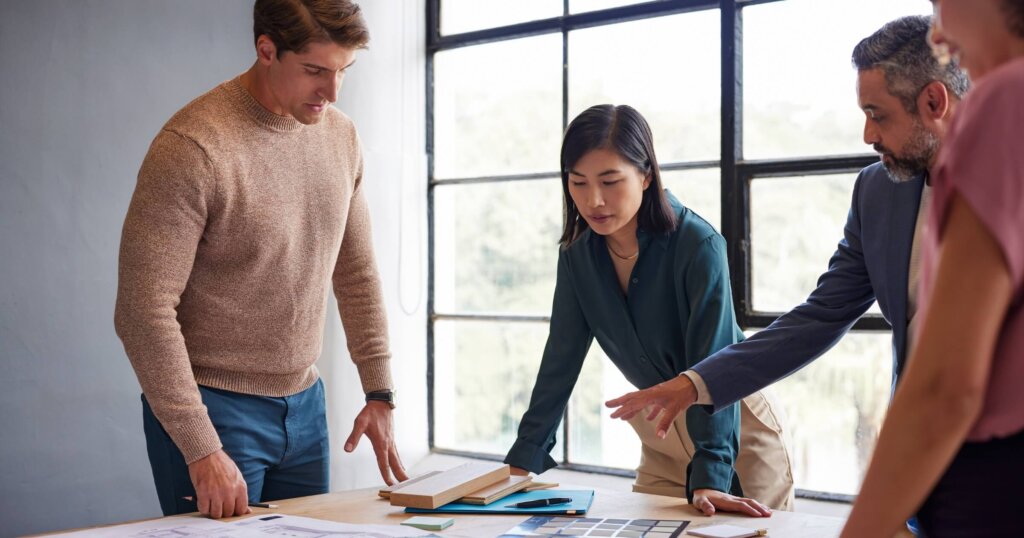 Chinese female architect discussing with multiethnic team while examining architectural plans and materials during a meeting. Casual architects and engineers discussing about building construction.