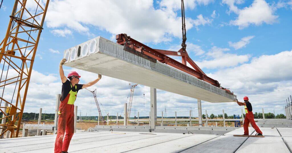 workers in safety protective equipment installing concrete floor slab panel at building construction site
