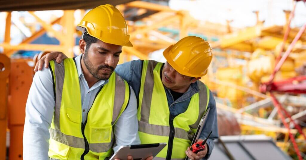 Asian man worker held tablet feeling sad and upset while sitting at construction site. Senior coworker wrapped around his shoulder and consoled him.