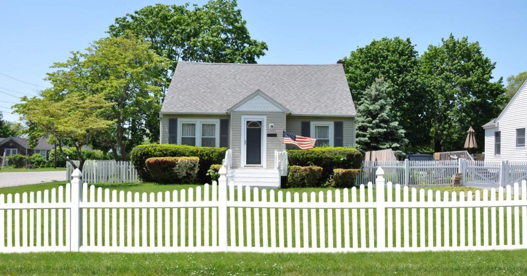 Gray Suburban Bungalow Home White Picket Fence Blue Sky USA.