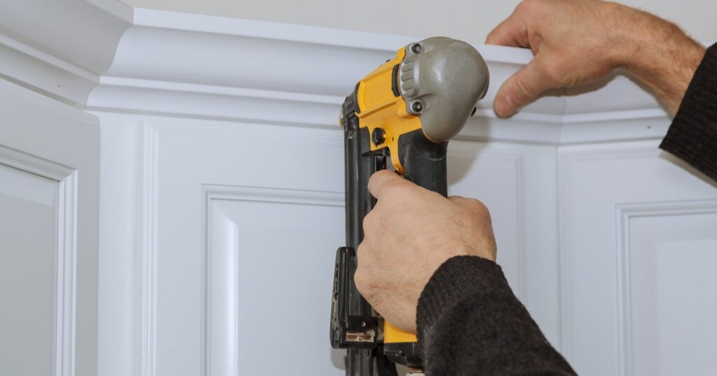 A worker using portable air gun nail in the nailing to crown moldings on new kitchen.
