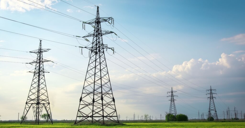 High voltage lines and power pylons in a flat and green agricultural landscape on a sunny day with clouds in the blue sky. Cloudy and rainy.