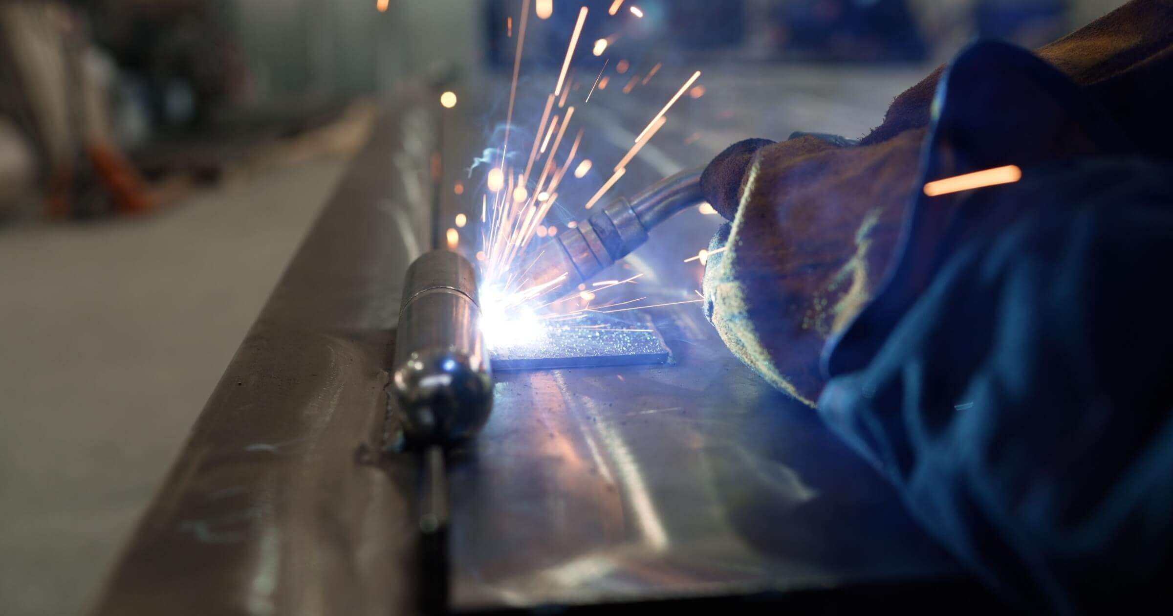 Welding with sparks close-up. Workers in industrial uniform and welded iron mask. Close-up of a welder welding metal. A welder in a mask welds metal and sparks the metal.