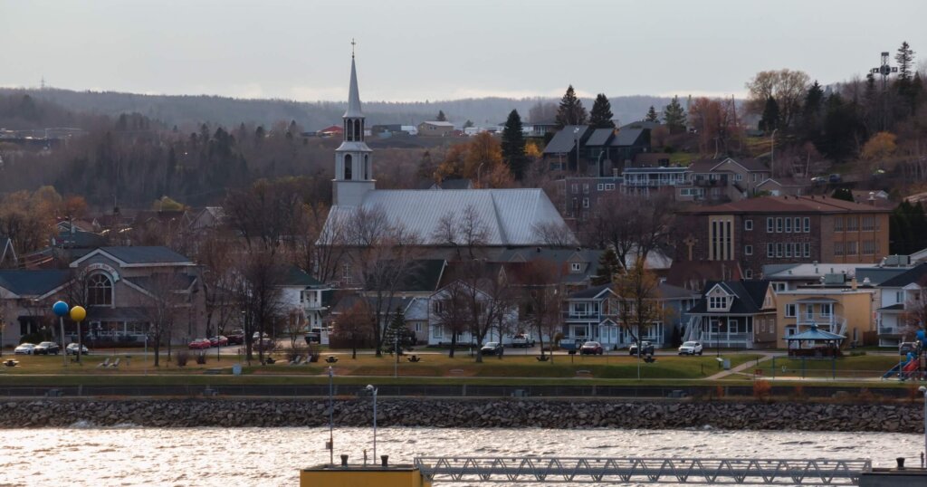 Saguenay, Quebec, Canada - Oct 30, 2024: Riverside view of Saguenay, Quebec, Canada as seen from the Saguenay River cruise ship terminal. Église St-Alphonse Church in view during autumn.