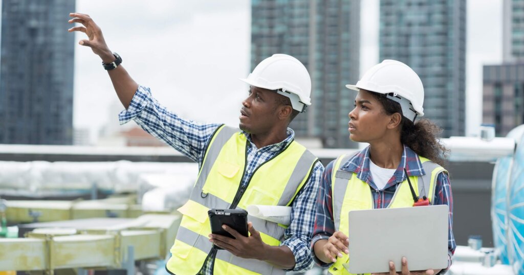 Male and female building inspectors working with laptop computer discuss and inspecting structure of building at rooftop of building at construction site.