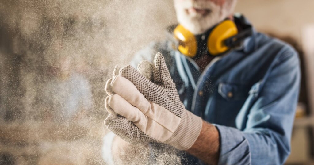Carpenter cleaning work gloves from sawdust after he finished processing the wood.