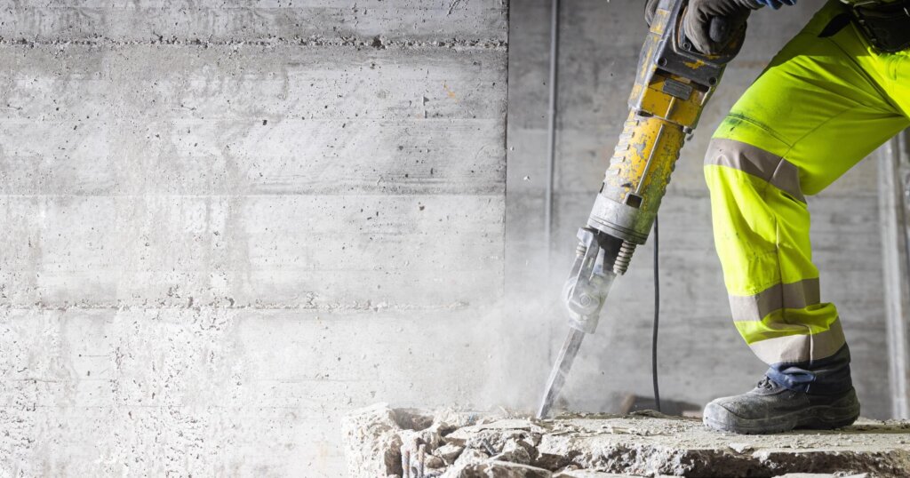 Construction worker using heavy-duty jackhammer tool and breaking reinforced concrete. Demolishing building interior. Under construction.