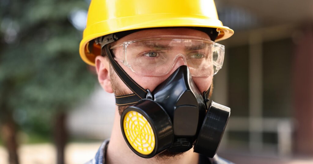 Man in respirator mask and hard hat outdoors. Safety equipment.