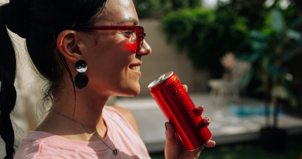 A girl on an orange background with a red energy drink can in her hands.