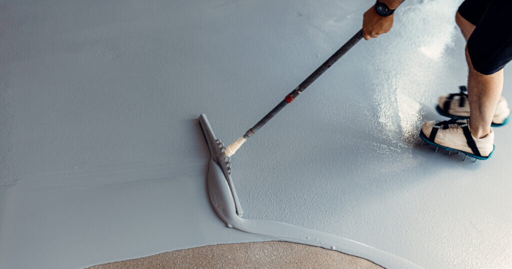 A construction worker apply grey epoxy resin in an industrial hall.