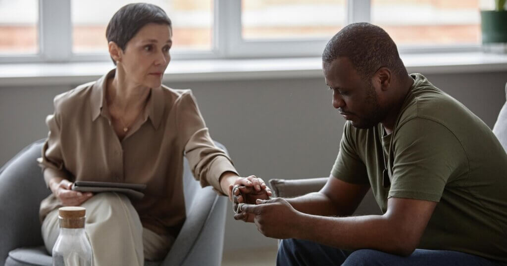 Side view portrait of emotional Black man as army veteran in therapy session with female psychologing supporting him in struggle copy space.