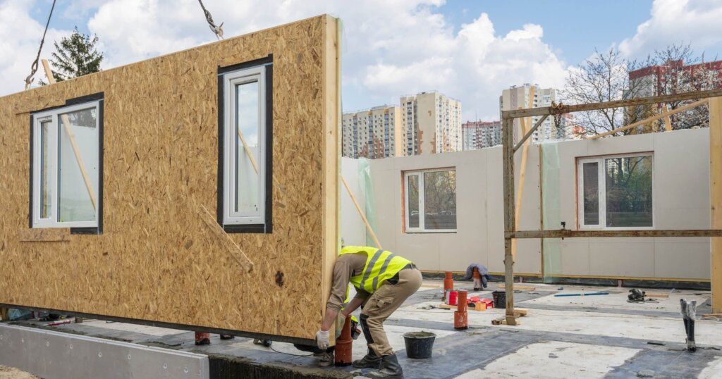 Process of construction new and modern modular house from composite sip panels. Worker man in special protective uniform wear working on building development industry of energy efficient property.