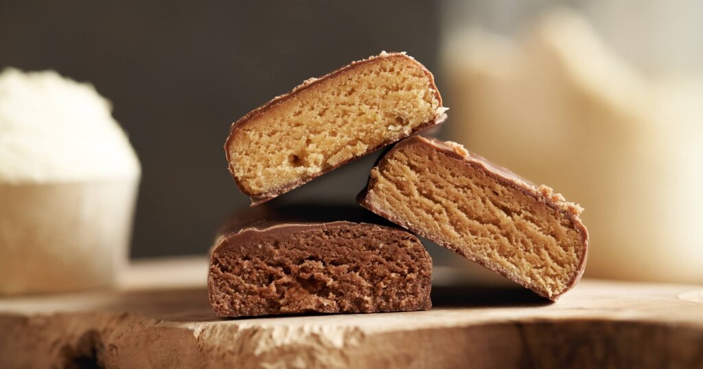 Three vegetarian protein chocolate bars with a jar of whey protein powder in the background.
