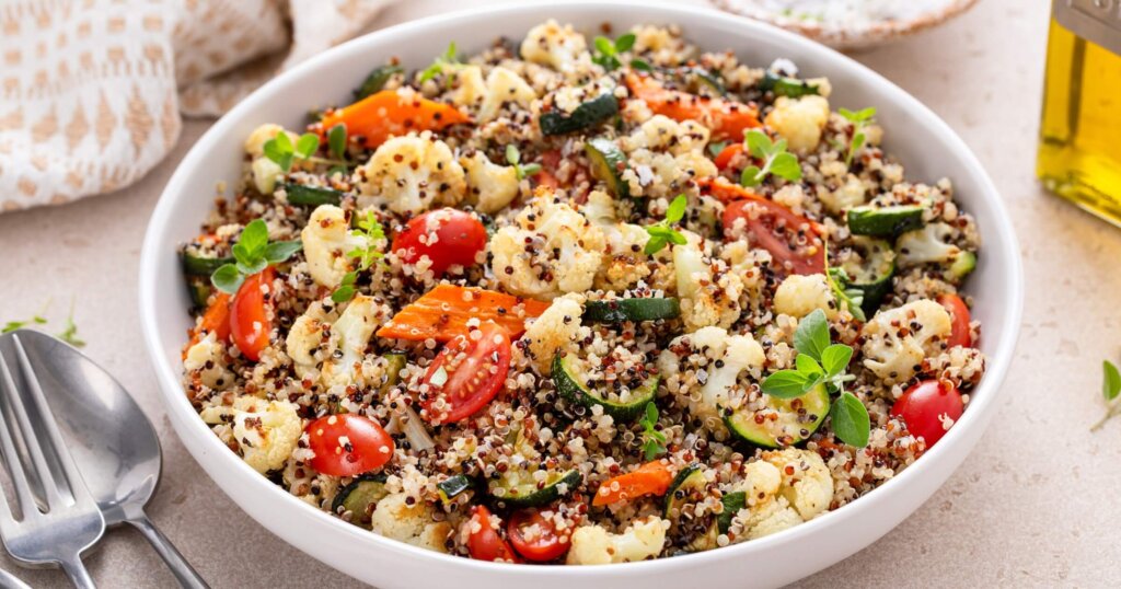 Delicious and nutritious quinoa salad with roasted vegetables, fresh tomatoes and herbs on a kitchen table.