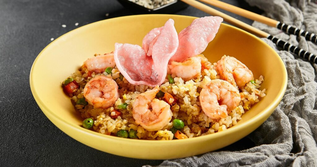Spicy Shrimp Fried Rice with Vegetables. Yellow plate with wooden chopstick on dark slate table. Chinese, asian, authentic food concept.