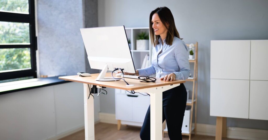 Woman Using Adjustable Height Standing Desk In Office For Good Posture.