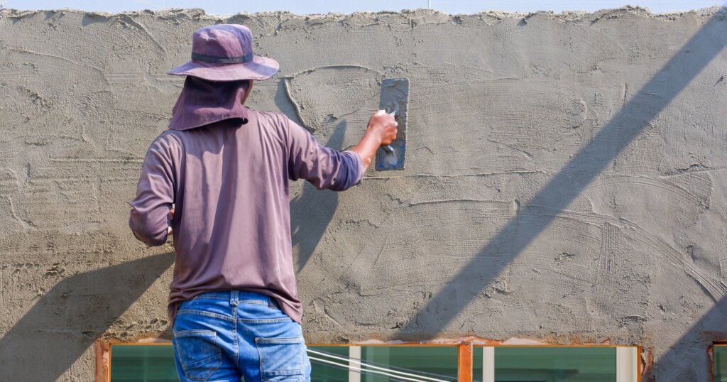 Builder worker using trowel to plastering cement on the wall while standing inside of house construction site, rear view with copy space.