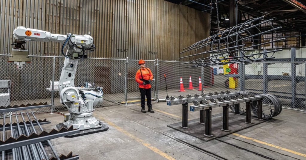 Toggle robotics robot working on rebard assembly. Worker in factory helping coordinate. 