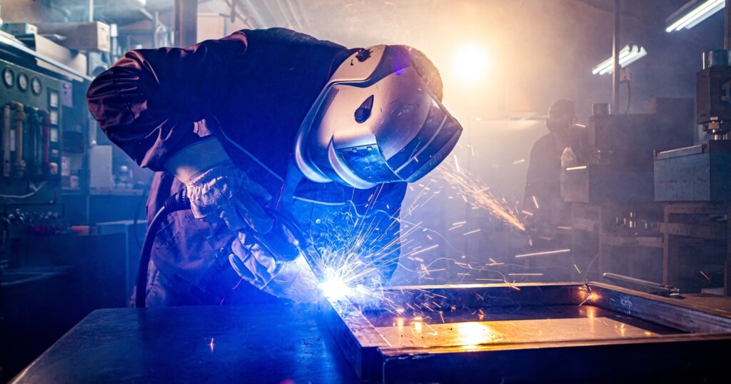 Worker with protective mask welding metal in workshop.