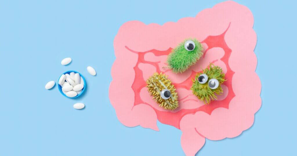 Cartoon intestinal model filled with cartoon bacteria and medicine pills on a blue background, concept gut health and probiotics