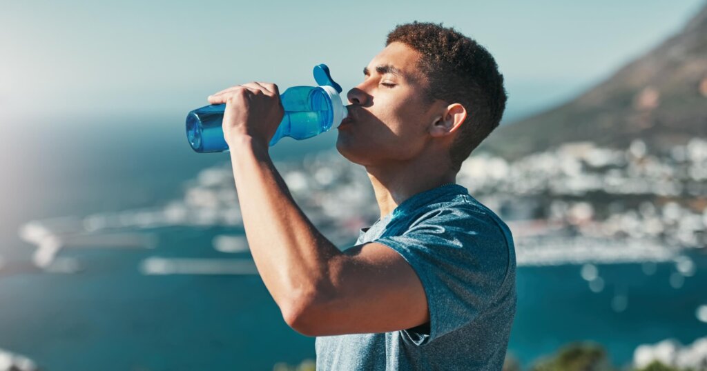 Fitness, man and drinking water outdoor for wellness, body health and nutrition benefits after exercise. Hydration, bottle and thirsty runner in nature with liquid for electrolytes on break or rest