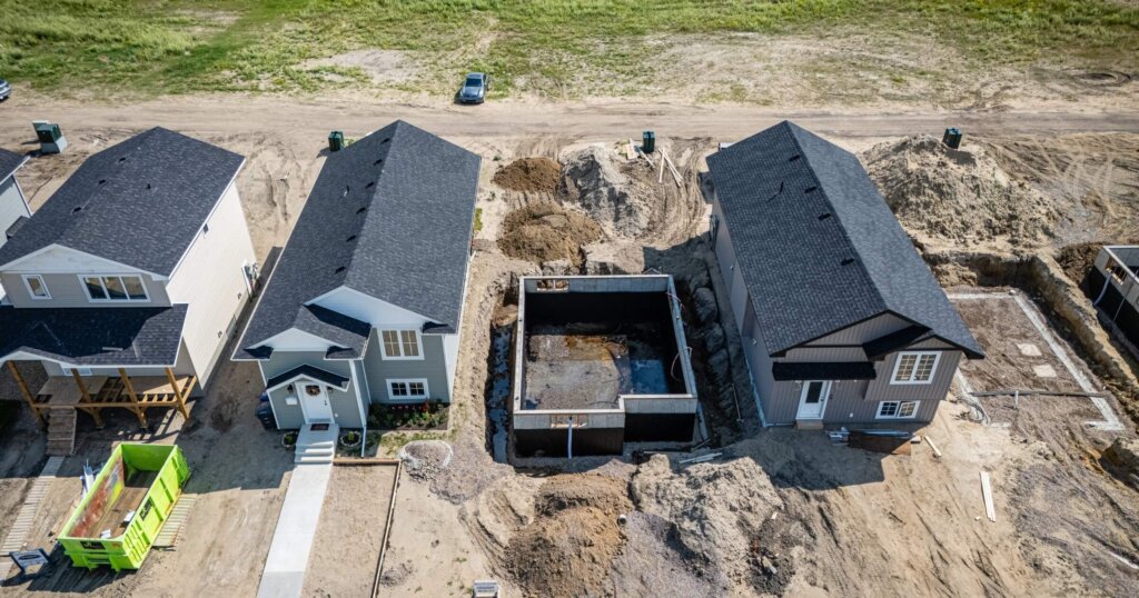 House is being constructed in front of another house. The construction site is small and he is in the process of being built.