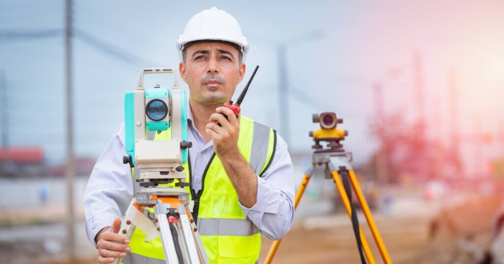 Surveyor engineer wearing safety uniform and helmet with equipment theodolite to measurement positioning and radio communication the construction site of the road with construct machinery background.