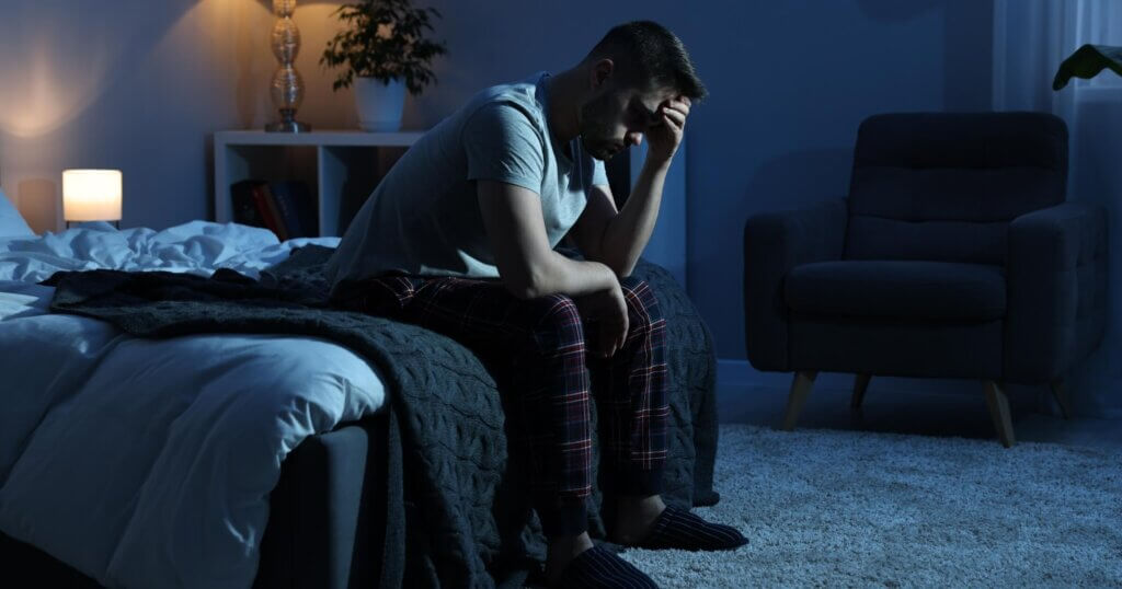 Frustrated man sitting on bed at night with anxiety.