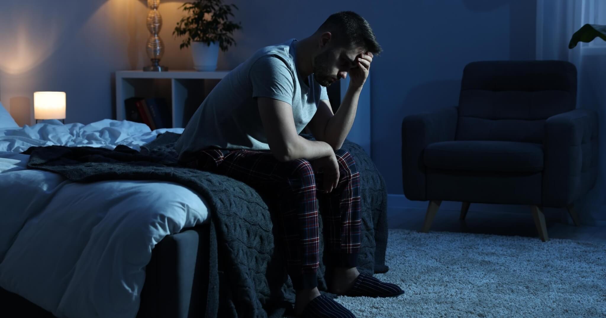 Frustrated man sitting on bed at night with anxiety.