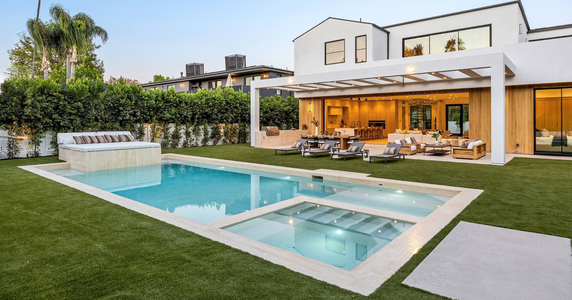 Modern luxury home with a spacious backyard, pool, and patio seating under a clear sky.