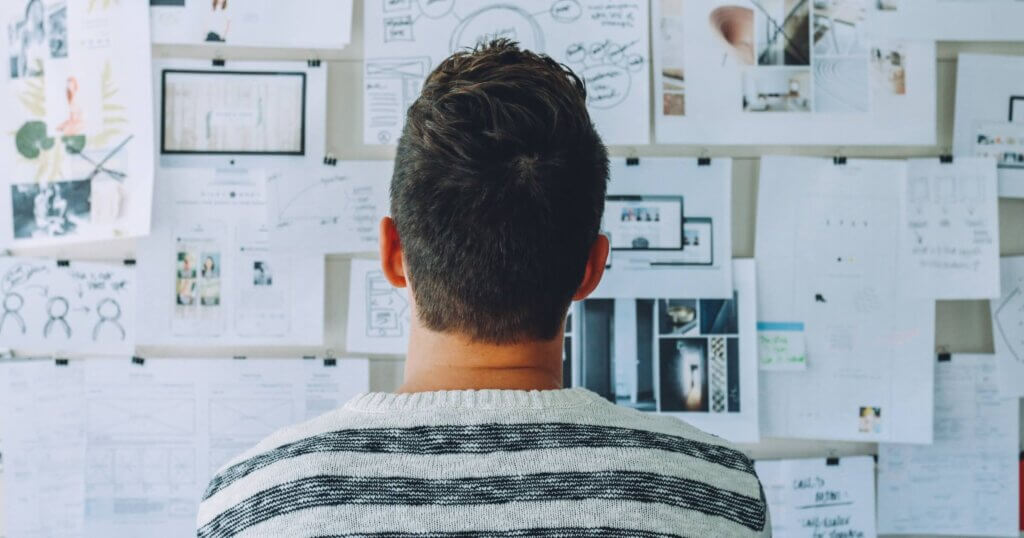 Man Wearing Black and White Stripe Shirt Looking at White Printer Papers on the Wall