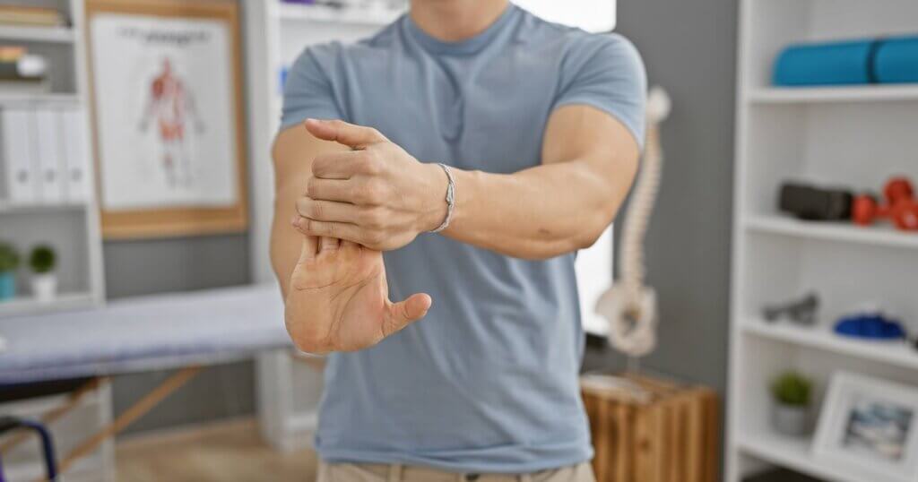 A young hispanic man stretching his wrist in a well-equipped rehabilitation clinic.