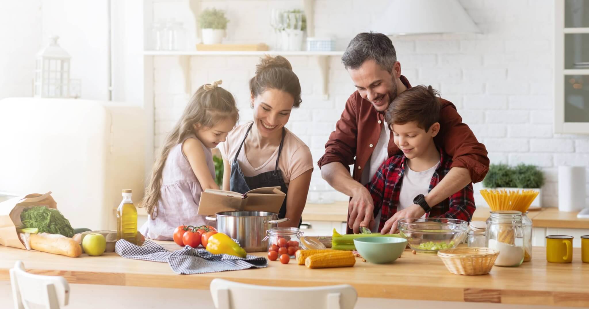 Happy family cooking a healthy dinner recipe together in kitchen. Mother and daughter reading recipe to father and son. Dad and boy chopping green vegetable leaf for salad. Home recreation and food preparation on weekend