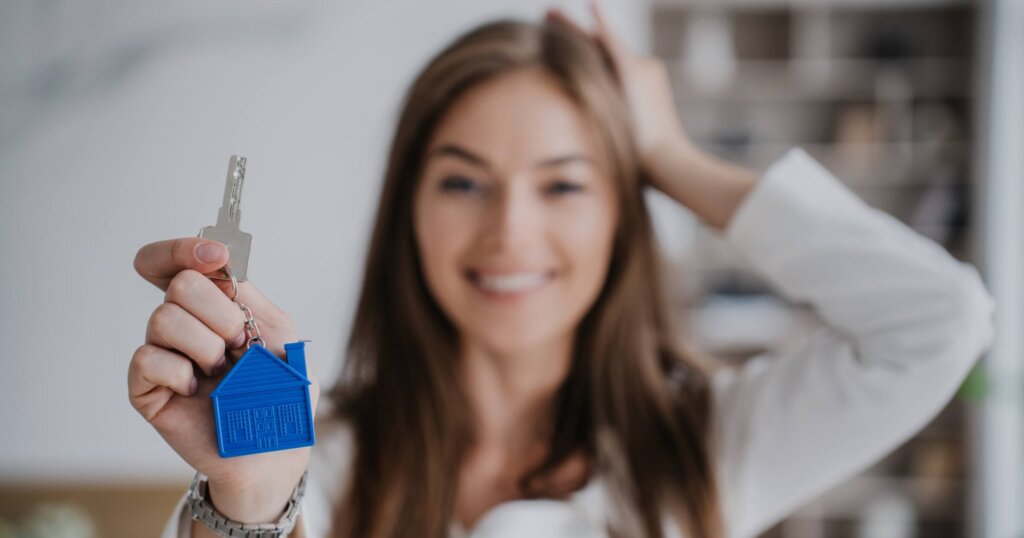 Women holding house key with blue keychain symbolizing homeownership.