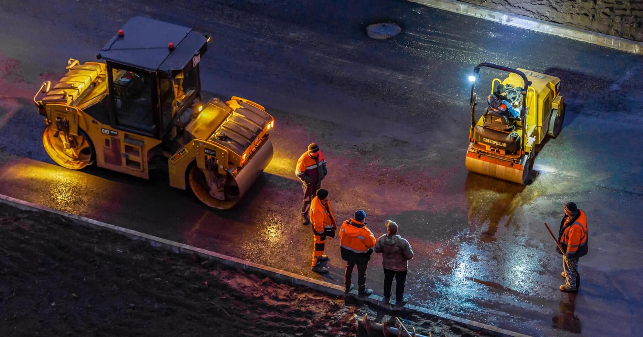 workers perform road work on laying asphalt on a city street at night. Road construction.