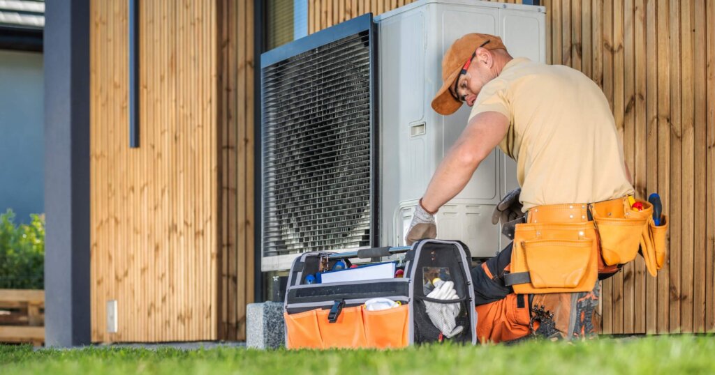 HVAC worker working on a modern heat pump outside a house.