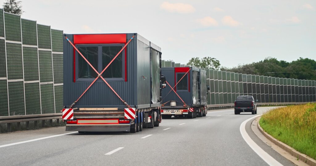 Large trucks carrying modular houses buildings on freeway