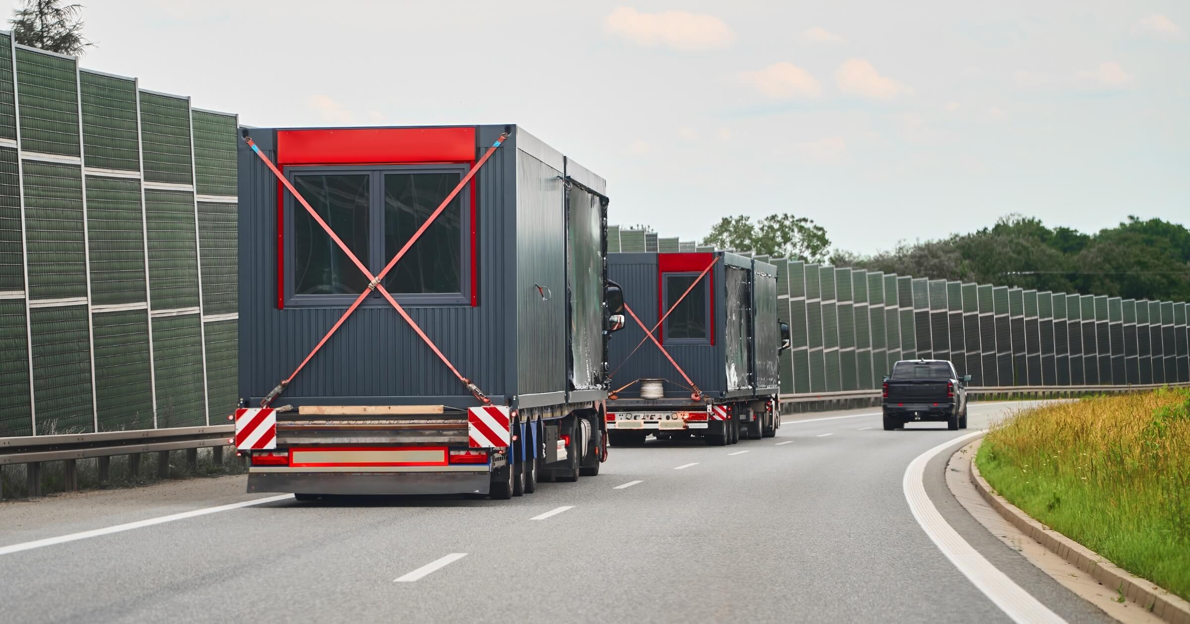 Large trucks carrying modular houses buildings on freeway