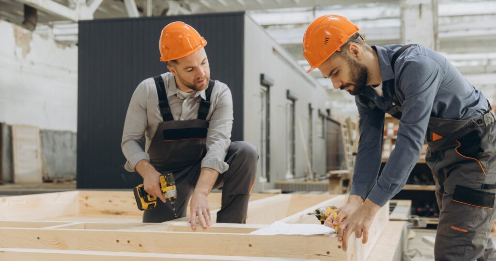 Two carpenters working on a wooden frame for prefabricated house