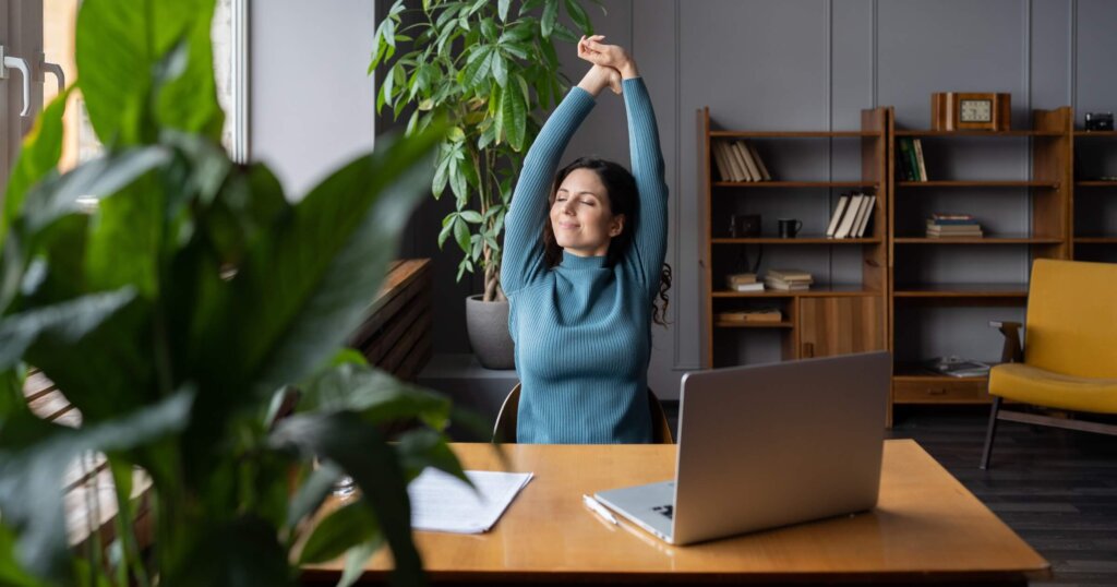 How to stay positive during difficult times at work: 12 habits that last 1 A woman enjoying a break stretches with a smile in an office setting.