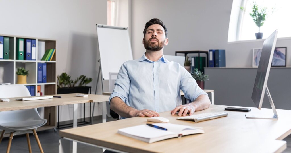 Businessman in the office with closed eyes performs breathing exercises, freelancer working on the computer.