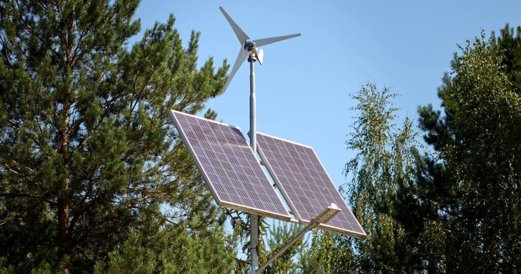 Solar panels and a small wind turbine installed outdoors, surrounded by trees, producing clean and renewable energy from sunlight and wind. Eco-friendly technology promoting sustainable generation.