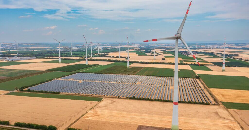 Bird's-eye view of solar panels in the middle of a wind farm.