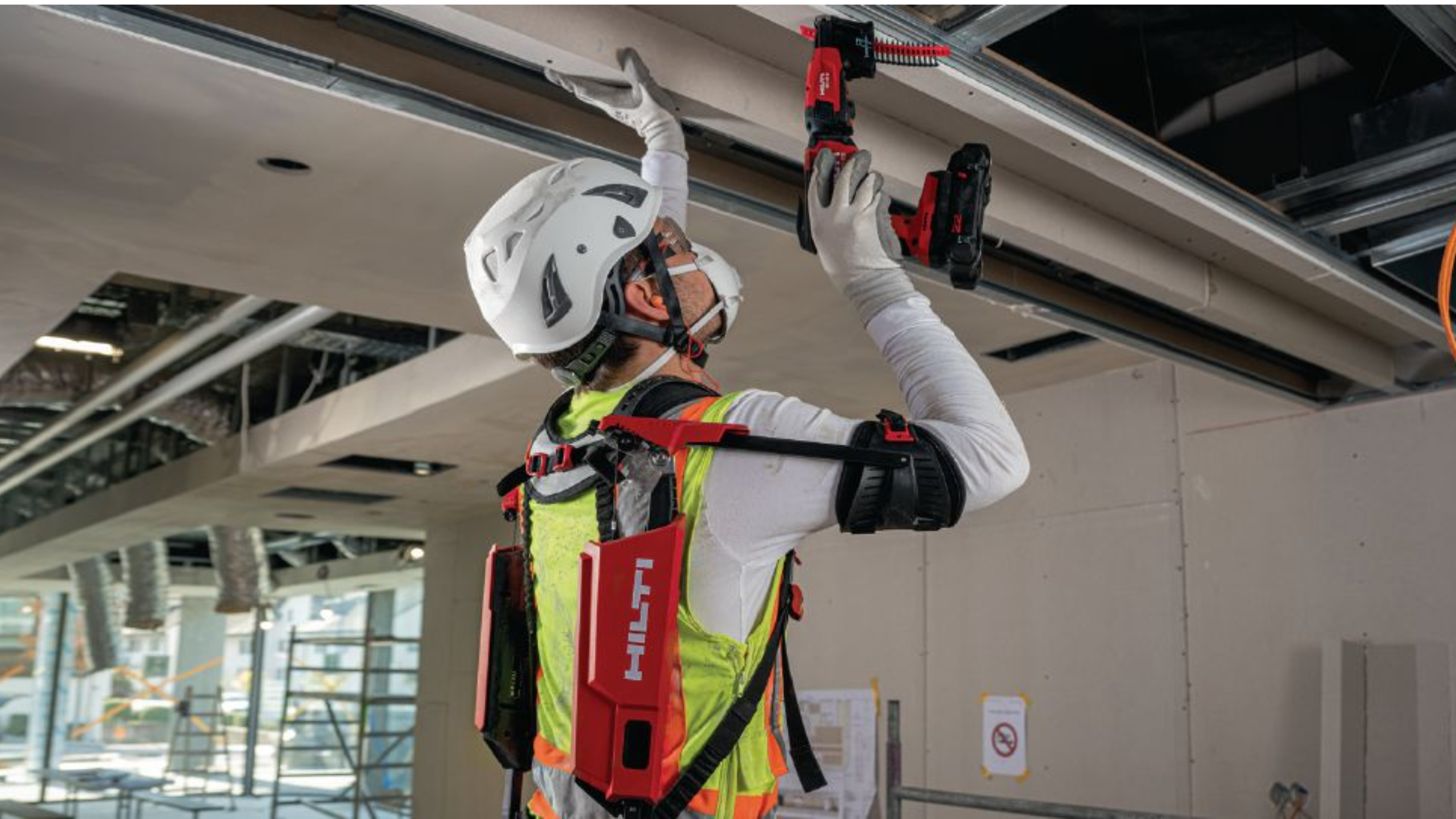 Construction worker using Hilti exoskeleton while drilling into ceiling