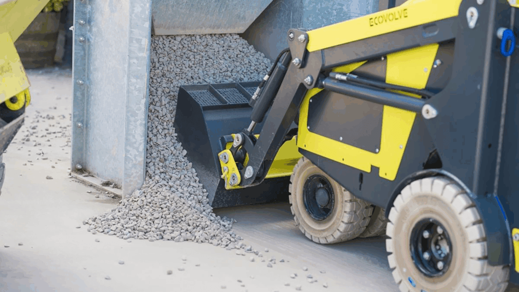 Ecovolve EL500 electric mini loader moving aggregate gravel with bucket attachment in confined outdoor space