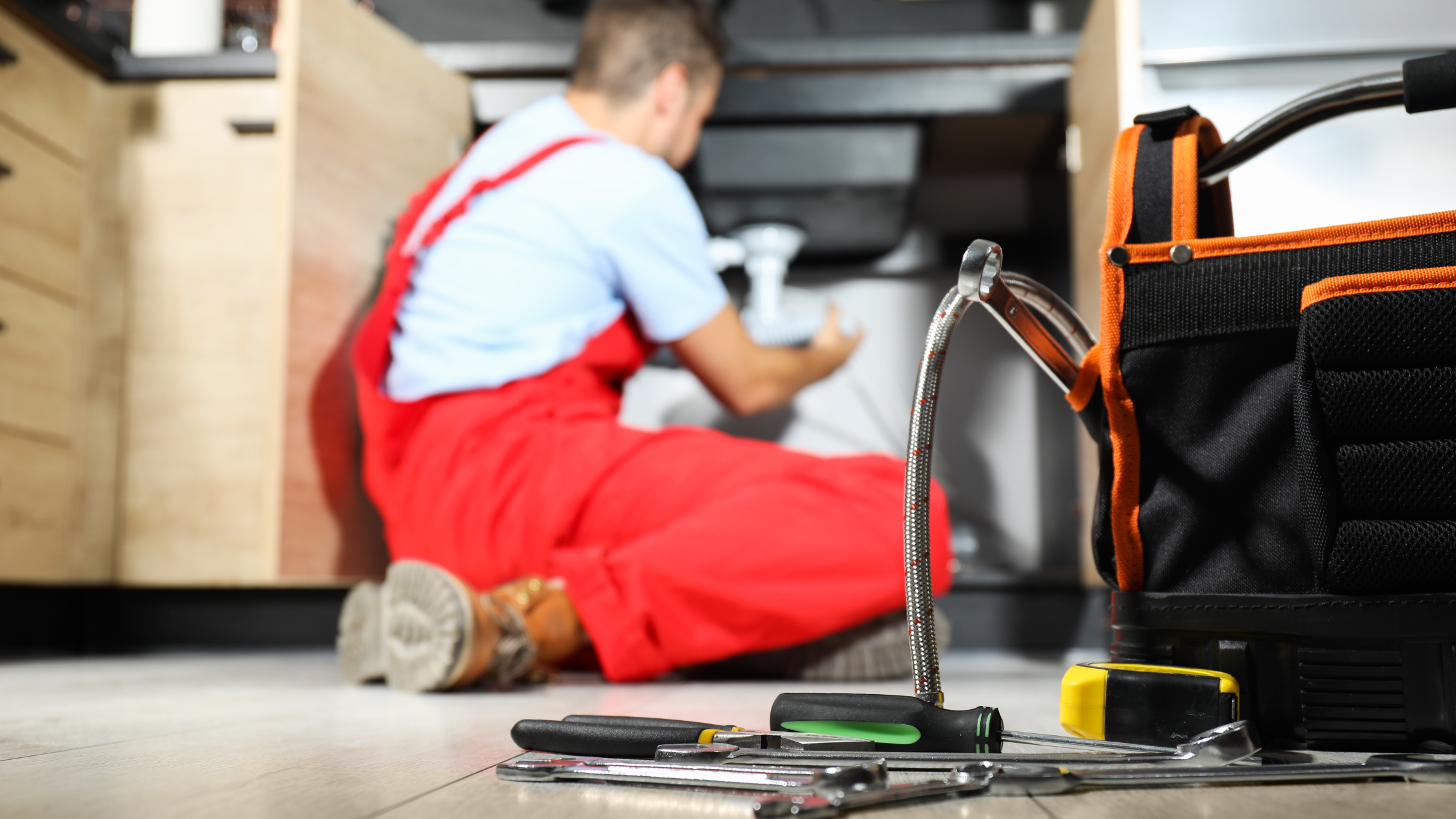 Plumber working under sink with tool bag