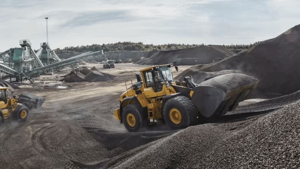 Volvo L150H wheel loader moving aggregate material at large scale aggregates plant with processing equipment and haul trucks in background